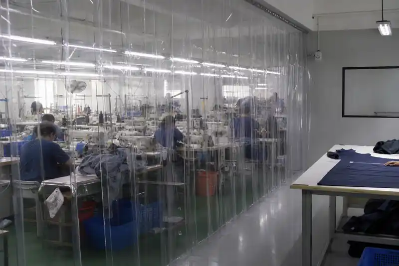 Thick transparent PVC strip curtains isolating sewing machine noise from an inspection area